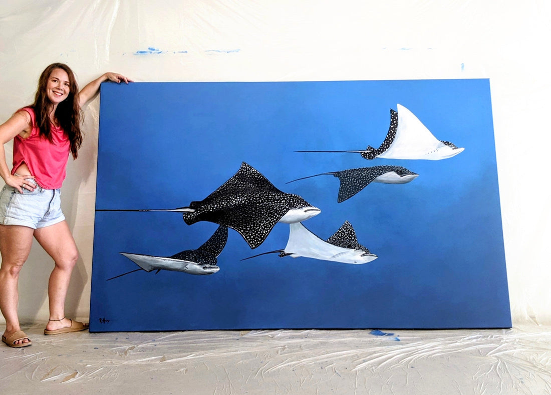 An Artist with her Painting of eagle rays in the blue ocean.