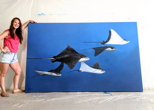 An Artist with her Painting of eagle rays in the blue ocean.