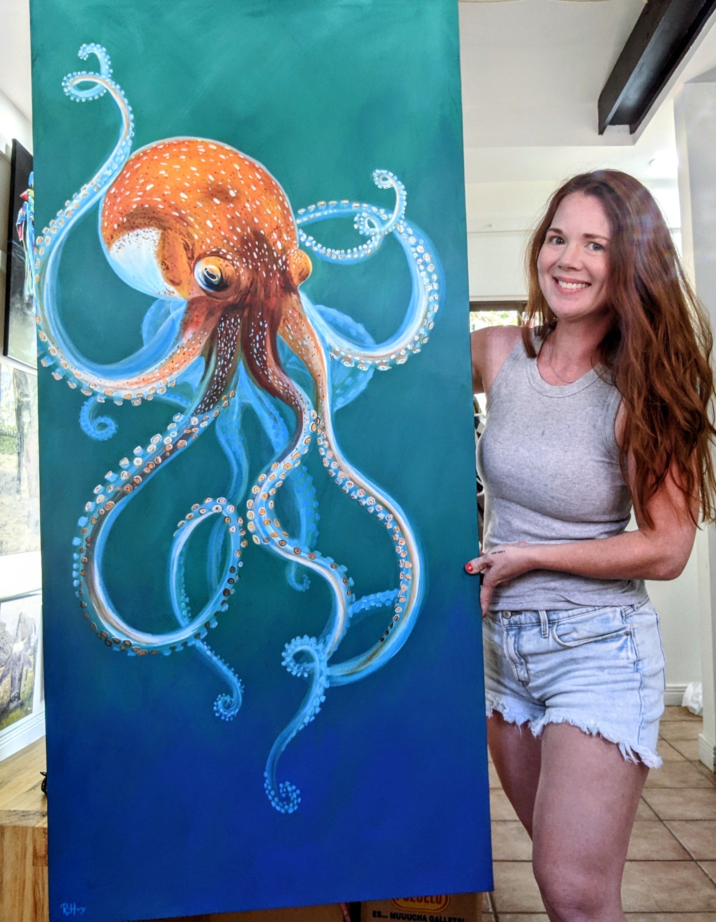 Wildlife Artist R Harvey with her painting of an orange octopus against an aqua and cobalt blue background.