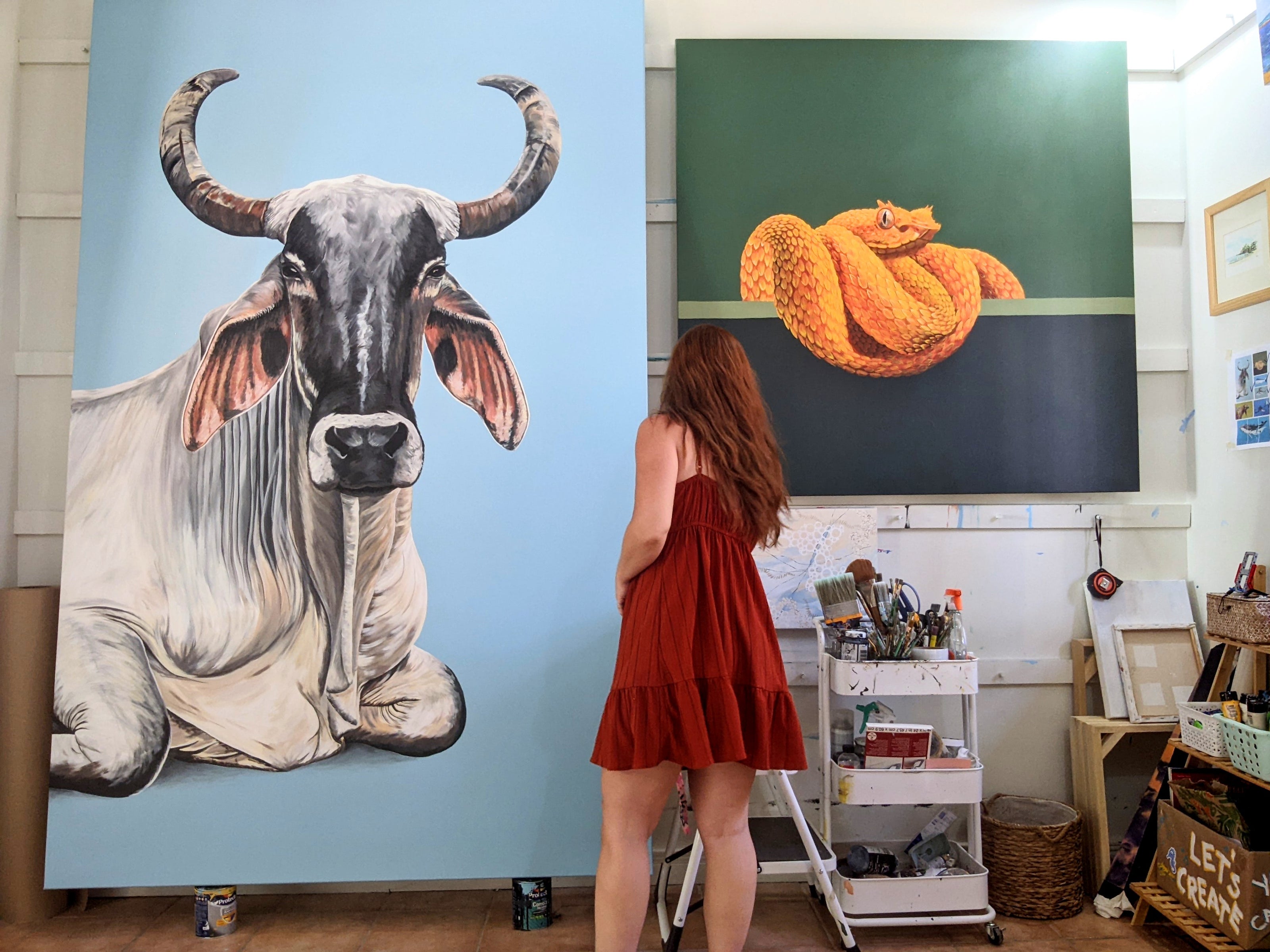 Wildlife Artist R Harvey in her art studio with 2 of her large paintings. One is of Celeste the cow and the other one is Sunshine the eyelash viper.
